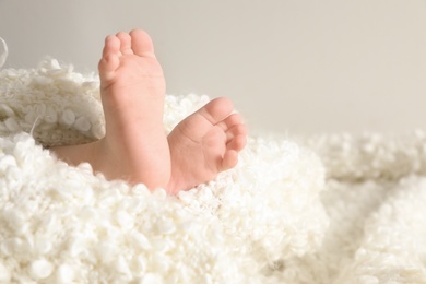 Photo of Little baby with cute feet wrapped in soft blanket against light background, closeup. Space for text