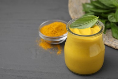 Tasty curry sauce, powder and basil leaves on grey wooden table. Space for text