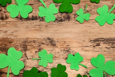 Decorative clover leaves on wooden table, flat lay with space for text. Saint Patrick's Day celebration