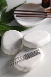Photo of Acupuncture needles and spa stones on white table