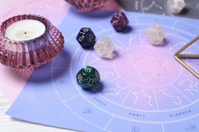 Photo of Zodiac wheel, astrology dices and burning candle on table, closeup