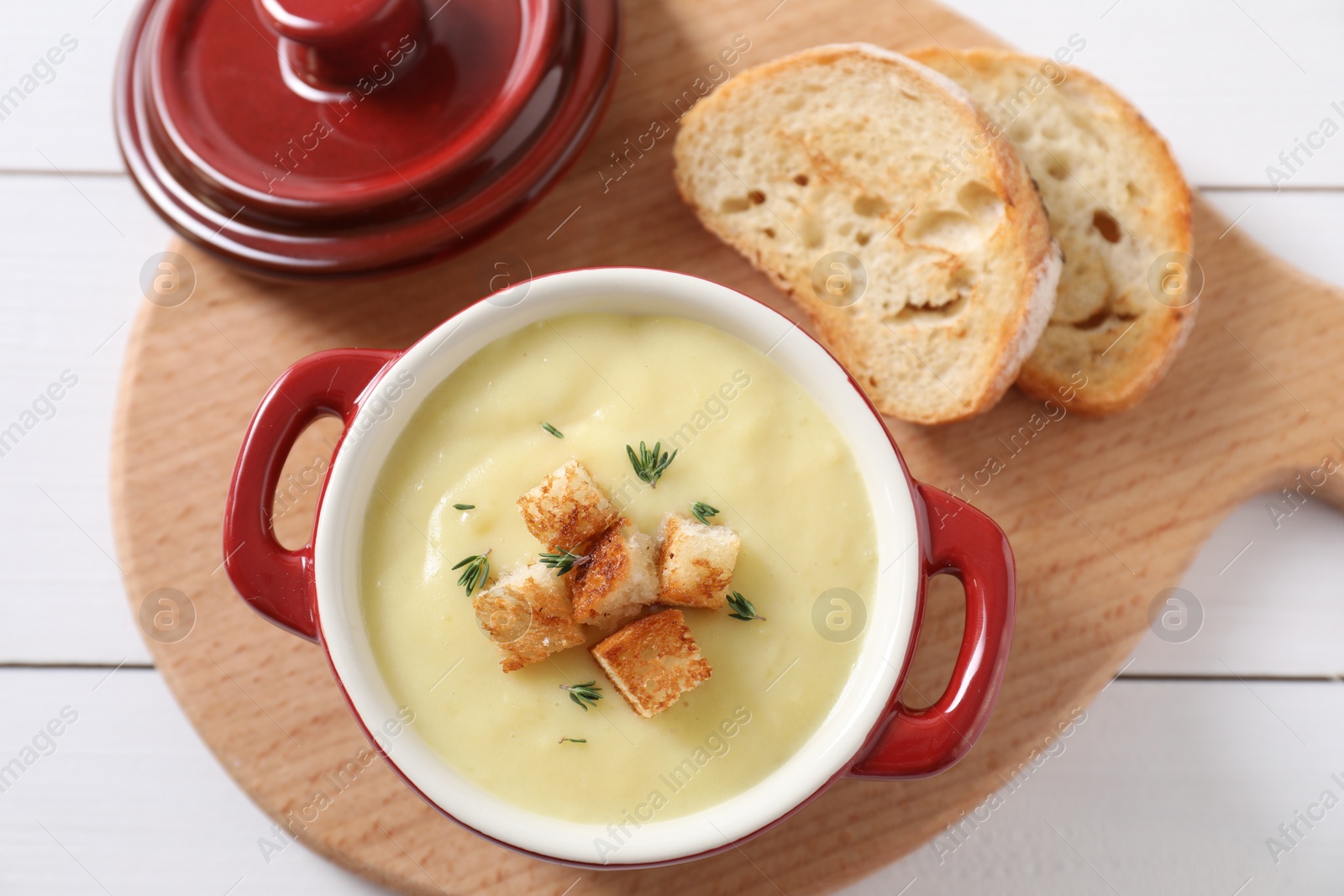 Photo of Tasty potato soup with croutons and rosemary in ceramic pot on white wooden table, flat lay