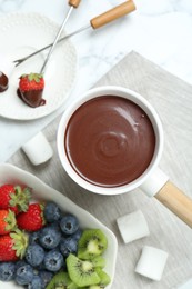 Photo of Fondue pot with melted chocolate, sweet marshmallows, fresh kiwi, different berries and forks on white marble table, flat lay