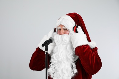 Photo of Santa Claus with headphones and microphone on light grey background. Christmas music