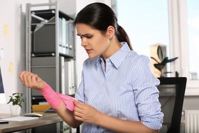 Photo of Young woman applying medical bandage onto wrist in office