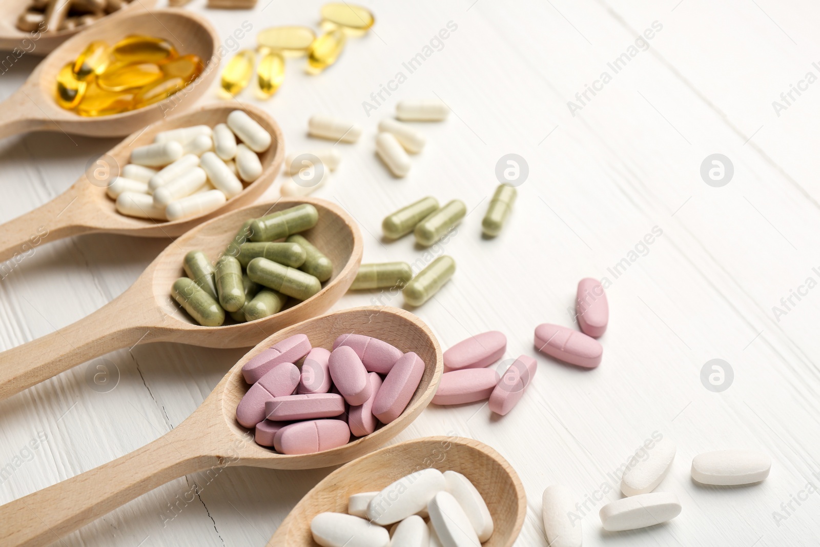 Photo of Different vitamin capsules in spoons on white wooden table, closeup. Space for text