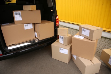 Photo of Black delivery van and many different parcels near yellow building outdoors. Courier service