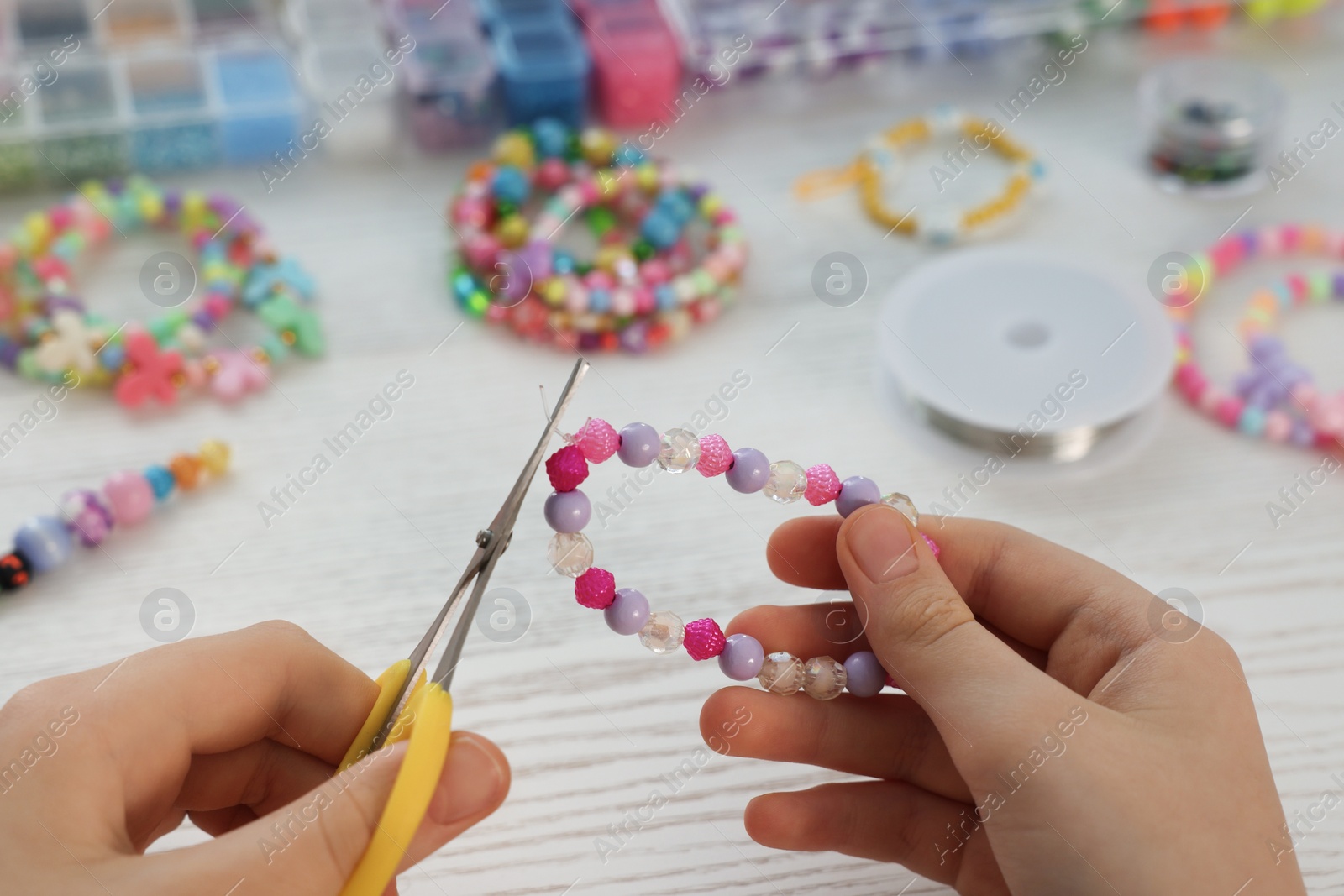 Photo of Girl making beaded jewelry at white wooden table, closeup