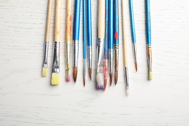 Different paint brushes on wooden background, top view