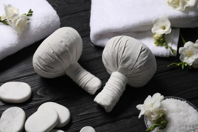 Composition with herbal massage bags and other spa products on black wooden table