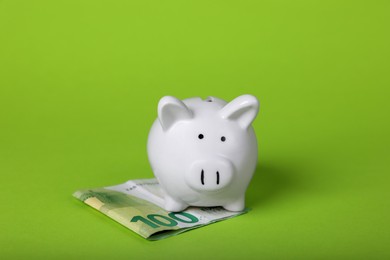 Photo of Ceramic piggy bank and euro banknote on light green background. Financial savings
