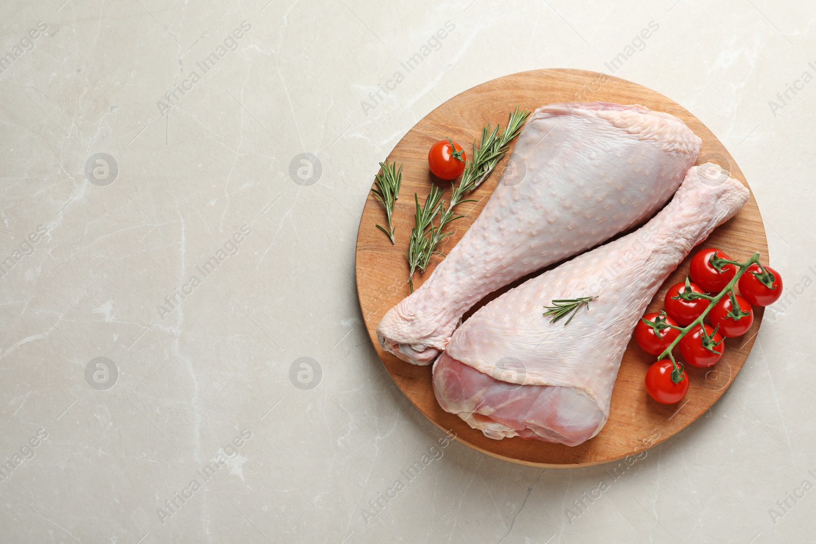 Photo of Board with raw turkey drumsticks, tomatoes and rosemary on light background, top view. Space for text