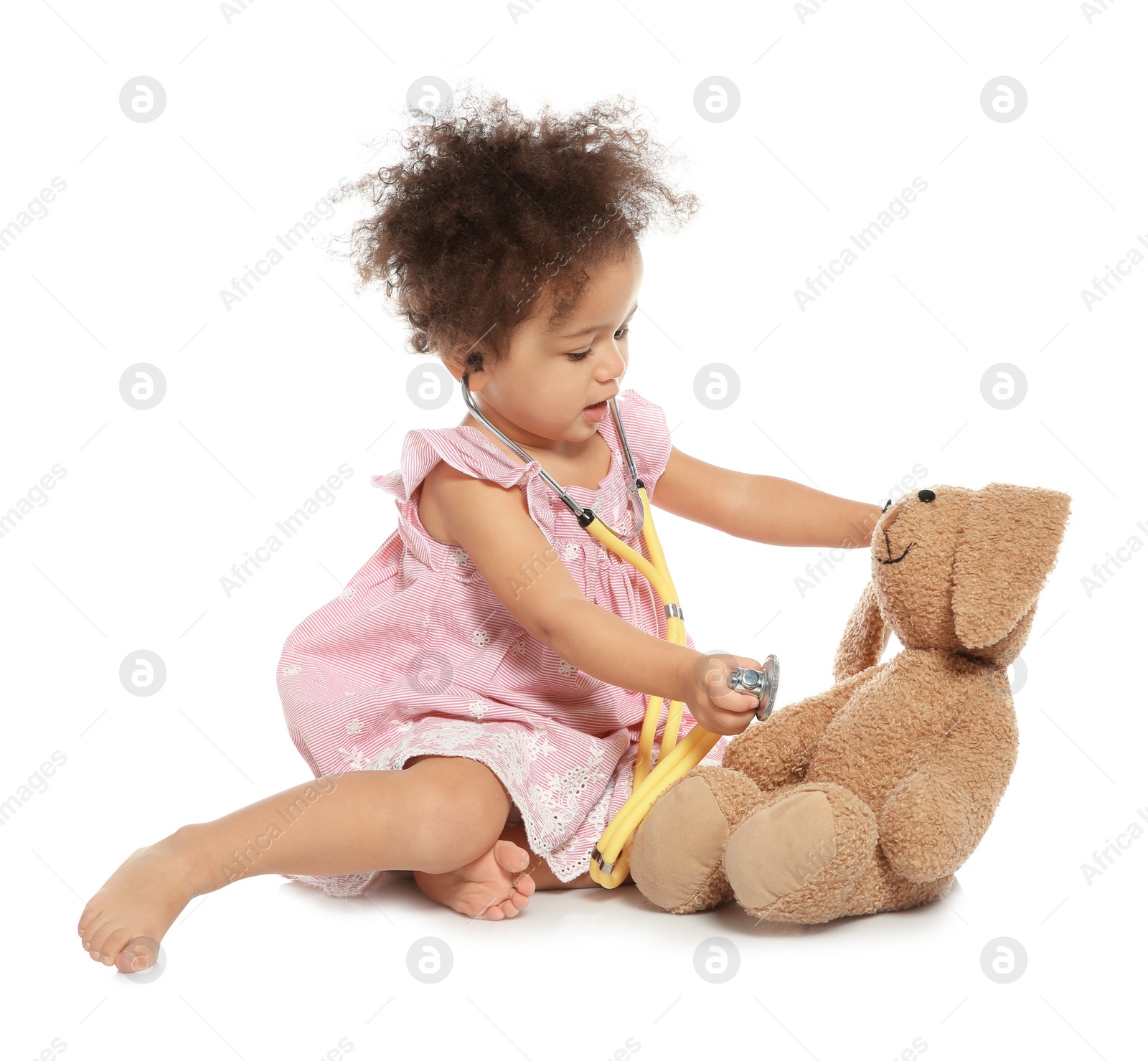 Photo of Cute African American child imagining herself as doctor while playing with stethoscope and toy bunny on white background