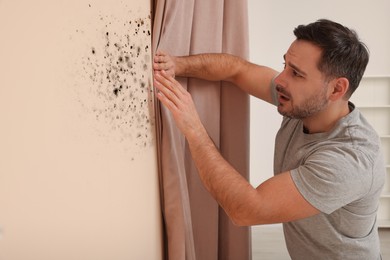 Image of Man looking at affected with mold wall in room