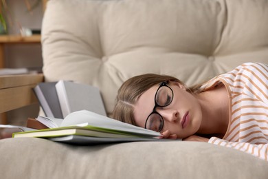 Young tired woman sleeping near books on couch indoors