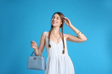 Beautiful young woman with stylish bag on light blue background