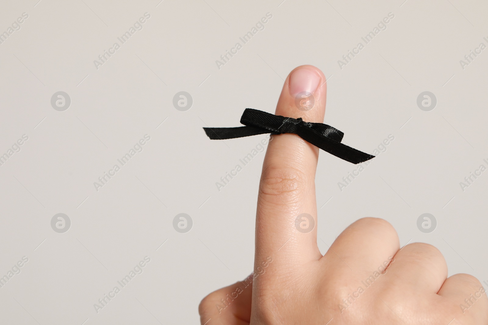 Photo of Man showing index finger with black tied bow as reminder on white background, closeup. Space for text