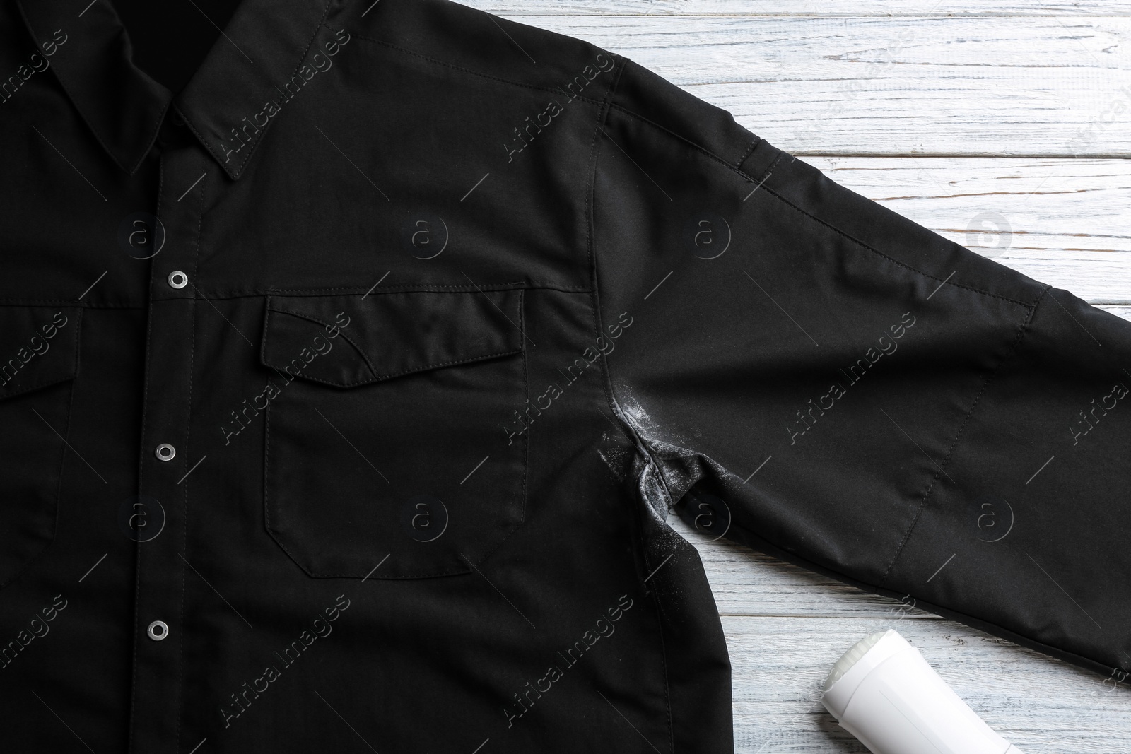 Photo of Black shirt with stain and deodorant on white wooden background, top view