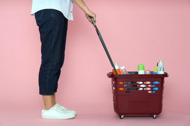 Photo of Woman with shopping basket full of cleaning supplies on pink background, closeup