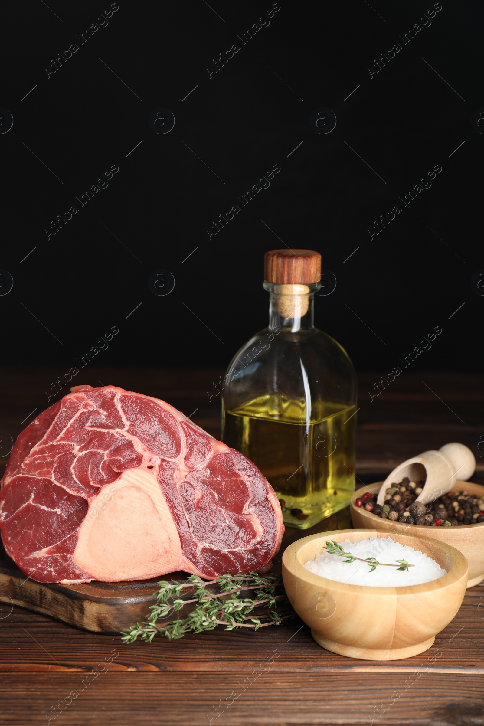 Photo of Piece of raw beef meat, thyme, oil and spices on wooden table against black background