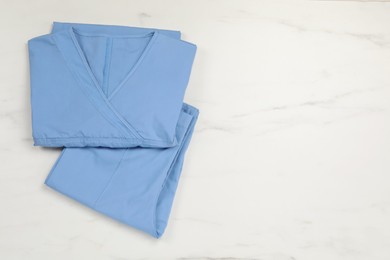 Photo of Light blue medical uniform on white marble table, top view. Space for text