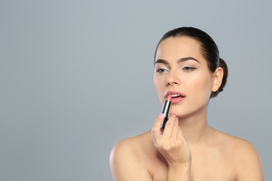 Photo of Young woman applying lipstick on color background. Space for text