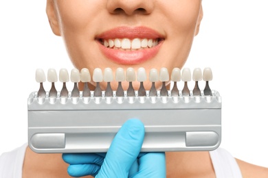 Photo of Doctor checking young woman's teeth color on white background, closeup. Cosmetic dentistry