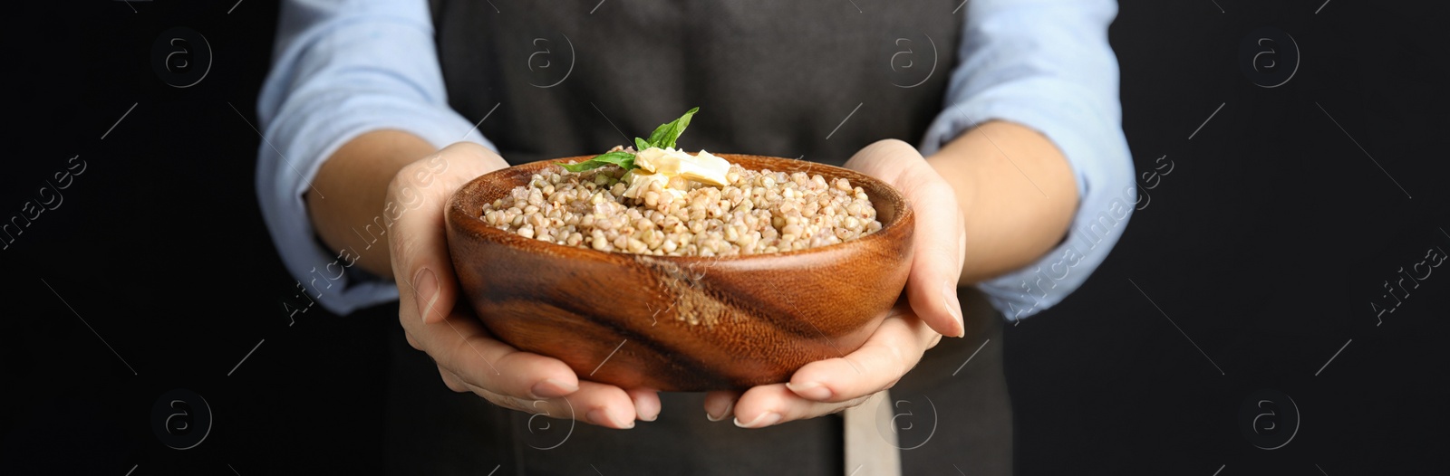 Image of Woman holding bowl with tasty buckwheat porridge on black background, closeup. Banner design