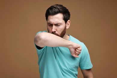 Photo of Sick man coughing into his elbow on brown background. Cold symptoms