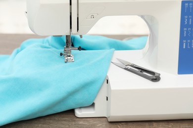 Photo of Sewing machine with fabric and tailor's scissors on wooden table indoors, closeup