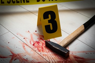 Hammer with blood and crime scene marker on white wooden background, closeup