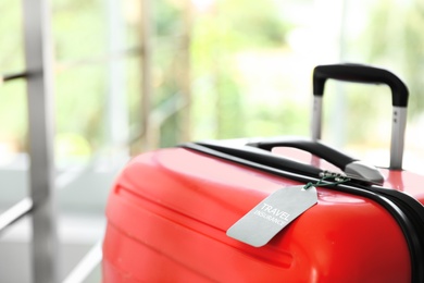 Photo of Stylish suitcase with travel insurance label on blurred background, closeup. Space for text