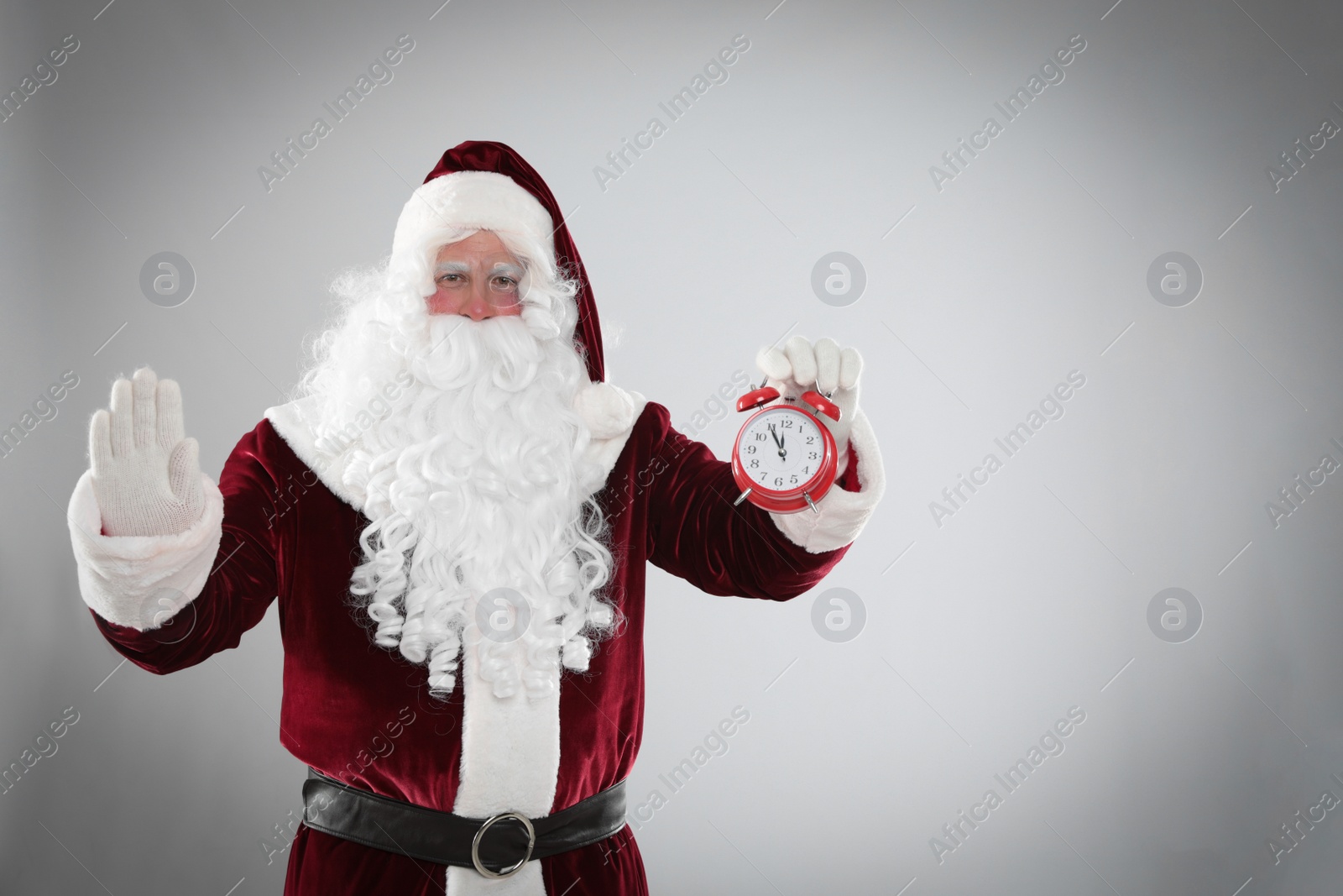 Photo of Santa Claus holding alarm clock on light grey background, space for text. Christmas countdown