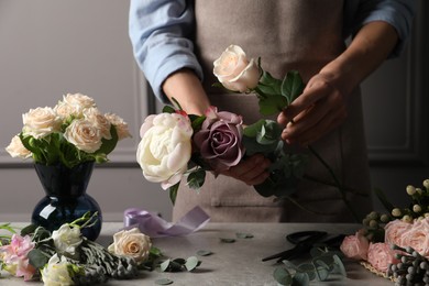 Photo of Florist creating beautiful bouquet at light grey table indoors, closeup