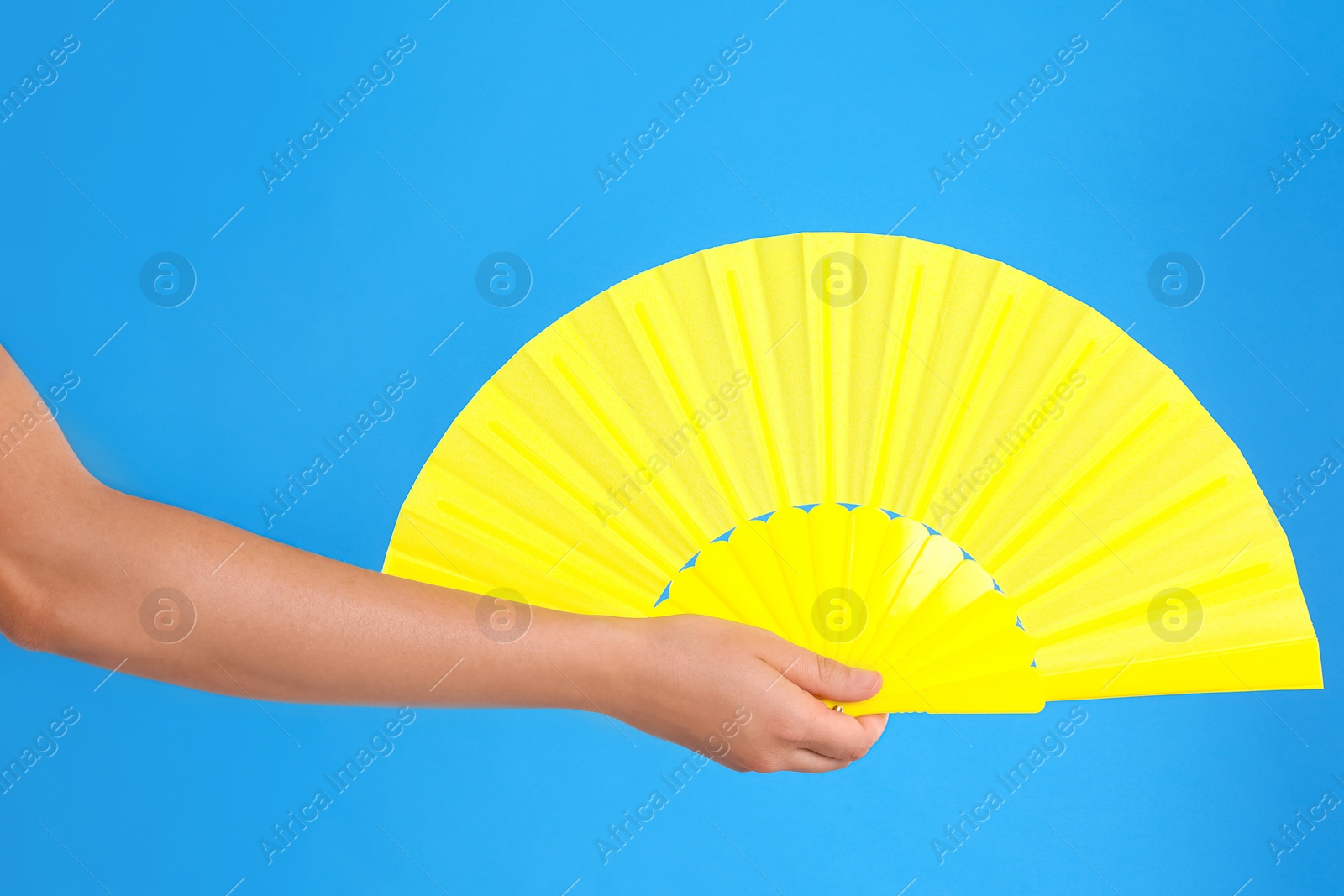 Photo of Woman holding yellow hand fan on light blue background, closeup