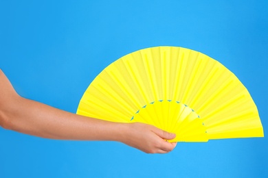 Photo of Woman holding yellow hand fan on light blue background, closeup