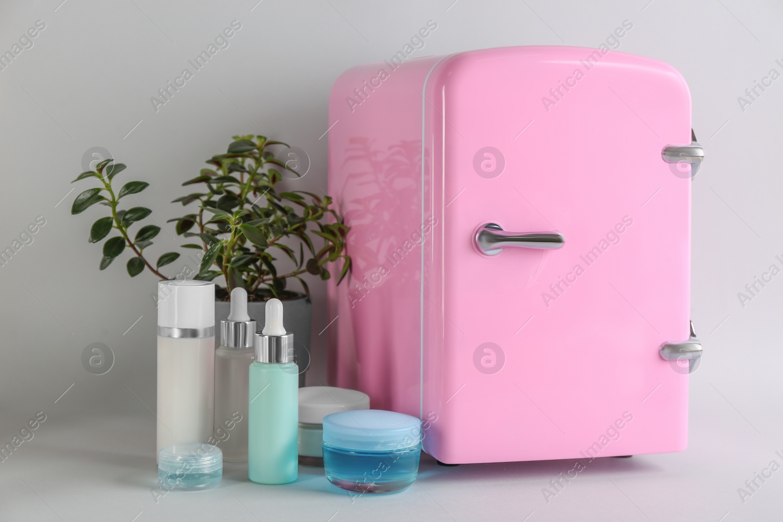 Photo of Cosmetic refrigerator and skin care products on light background