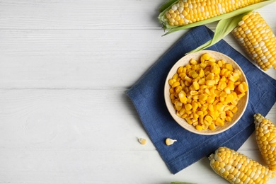 Photo of Tasty sweet corn kernels in bowl and fresh cobs on white wooden table, flat lay. Space for text