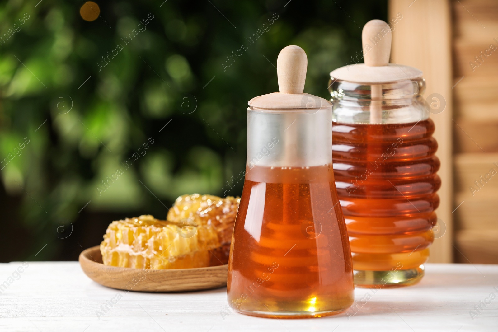 Photo of Tasty honey on table against green blurred background