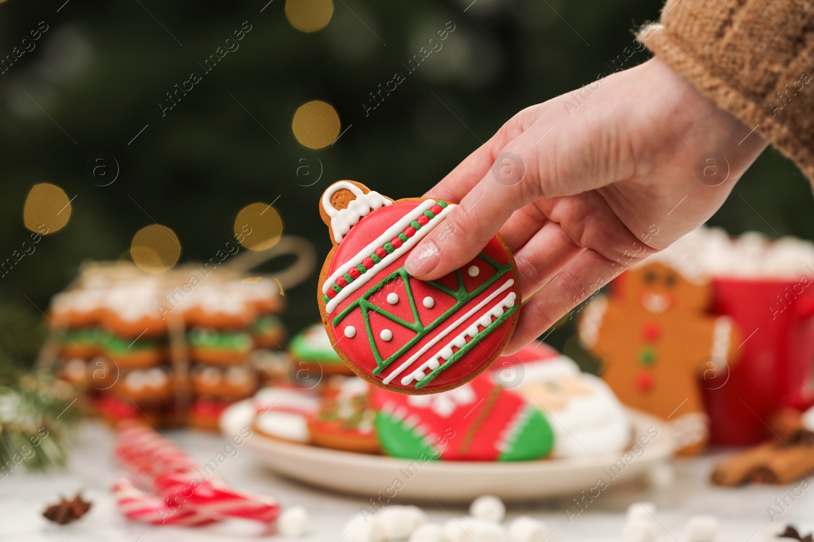 Photo of Woman with decorated cookie at table against blurred Christmas lights, closeup