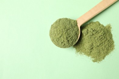 Photo of Wheat grass powder and spoon on green table, top view. Space for text