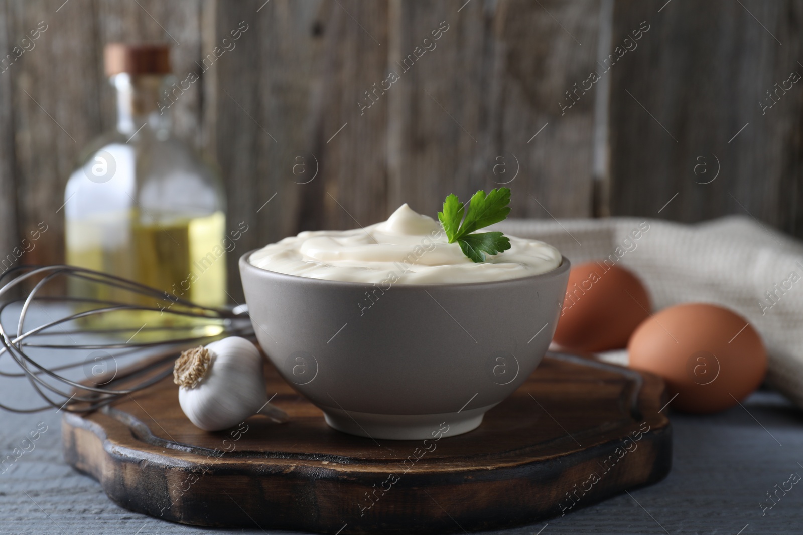 Photo of Tasty mayonnaise in bowl and ingredients on light grey wooden table, closeup