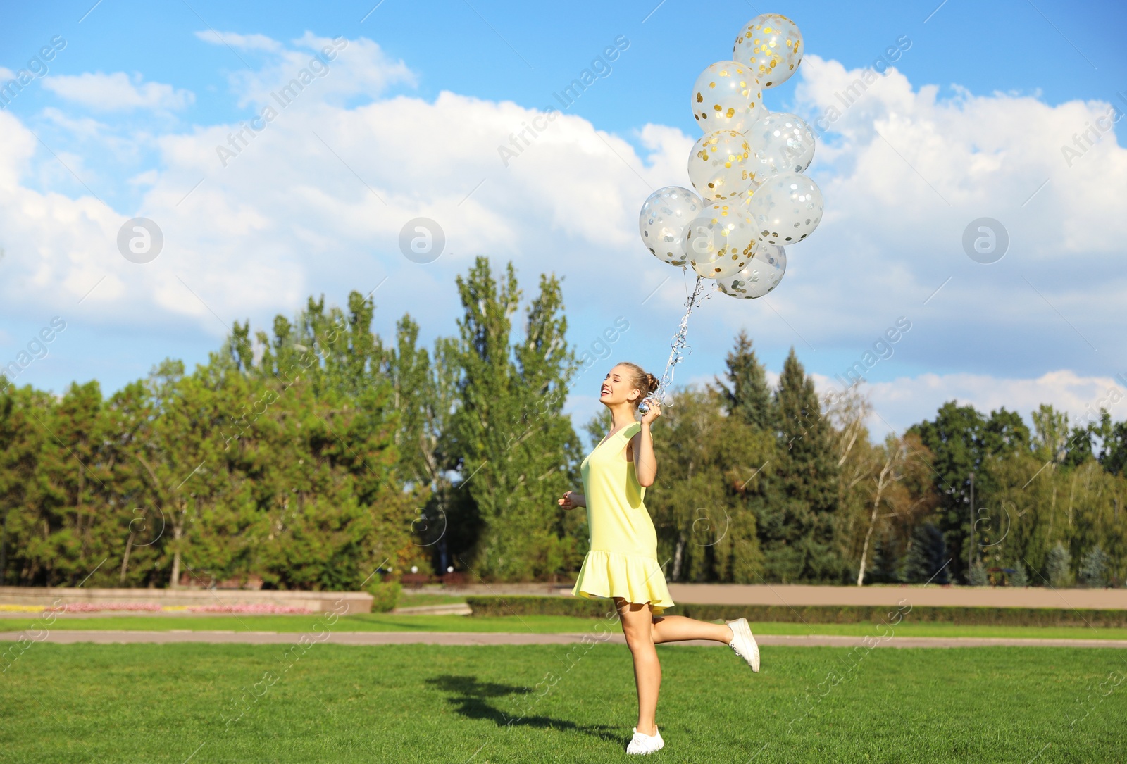 Photo of Beautiful young woman holding glitter balloons in park