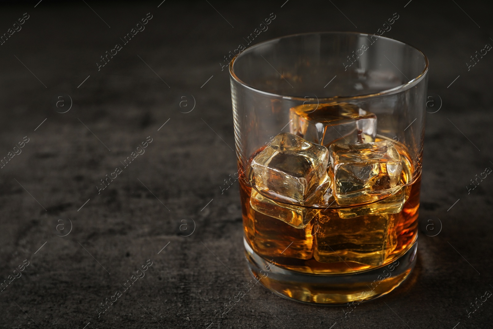 Photo of Golden whiskey in glass with ice cubes on table. Space for text