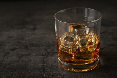 Golden whiskey in glass with ice cubes on table. Space for text