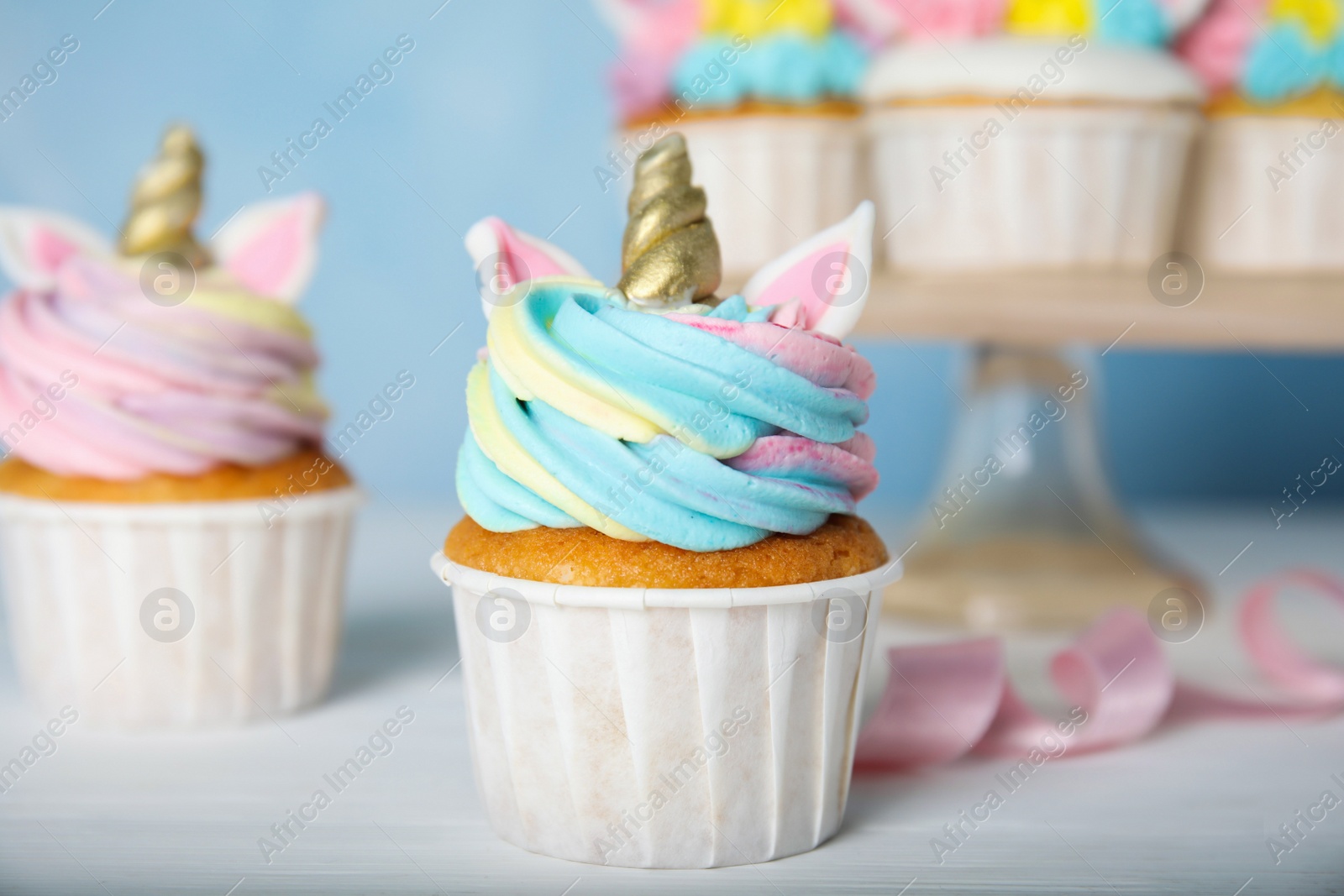 Photo of Cute sweet unicorn cupcakes on white wooden table, closeup