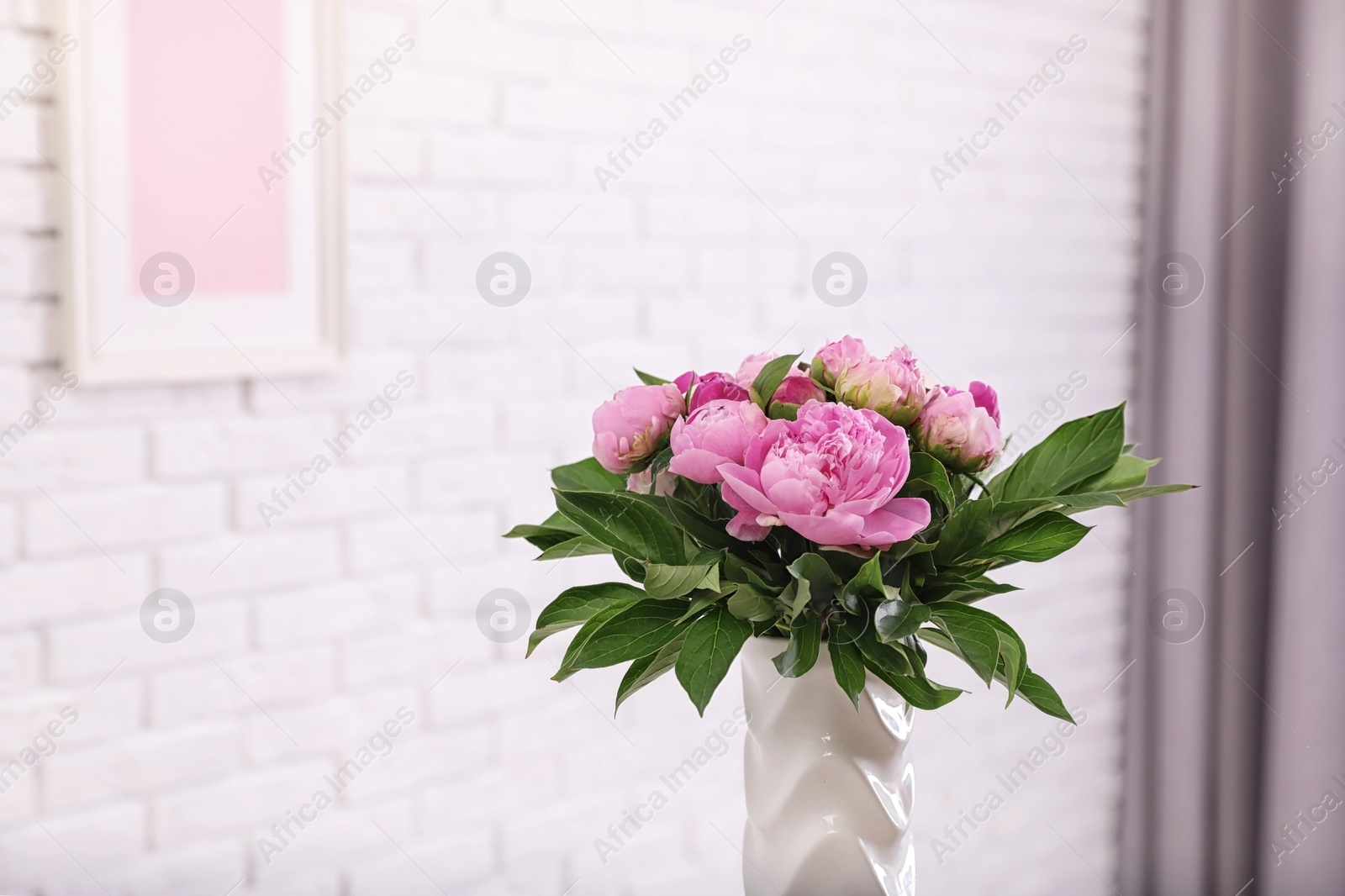 Photo of Vase with bouquet of beautiful peonies at white wall in room, space for text