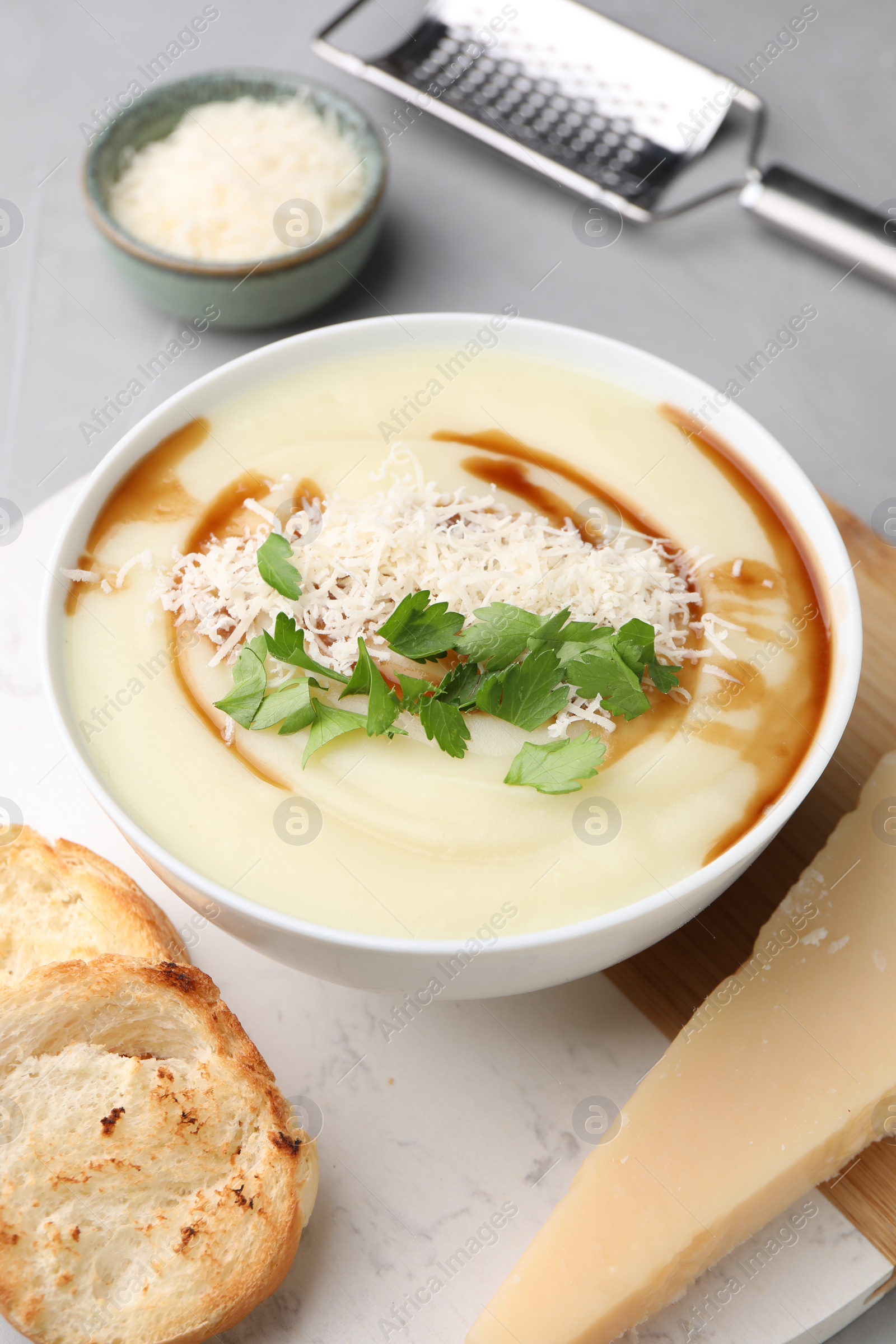 Photo of Delicious cream soup with parmesan cheese, soy sauce in bowl and croutons on light grey table