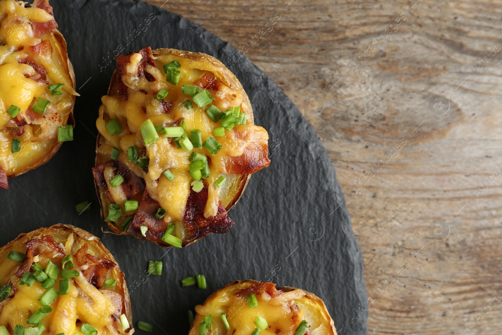 Photo of Slate plate with baked potatoes on wooden background, top view with space for text