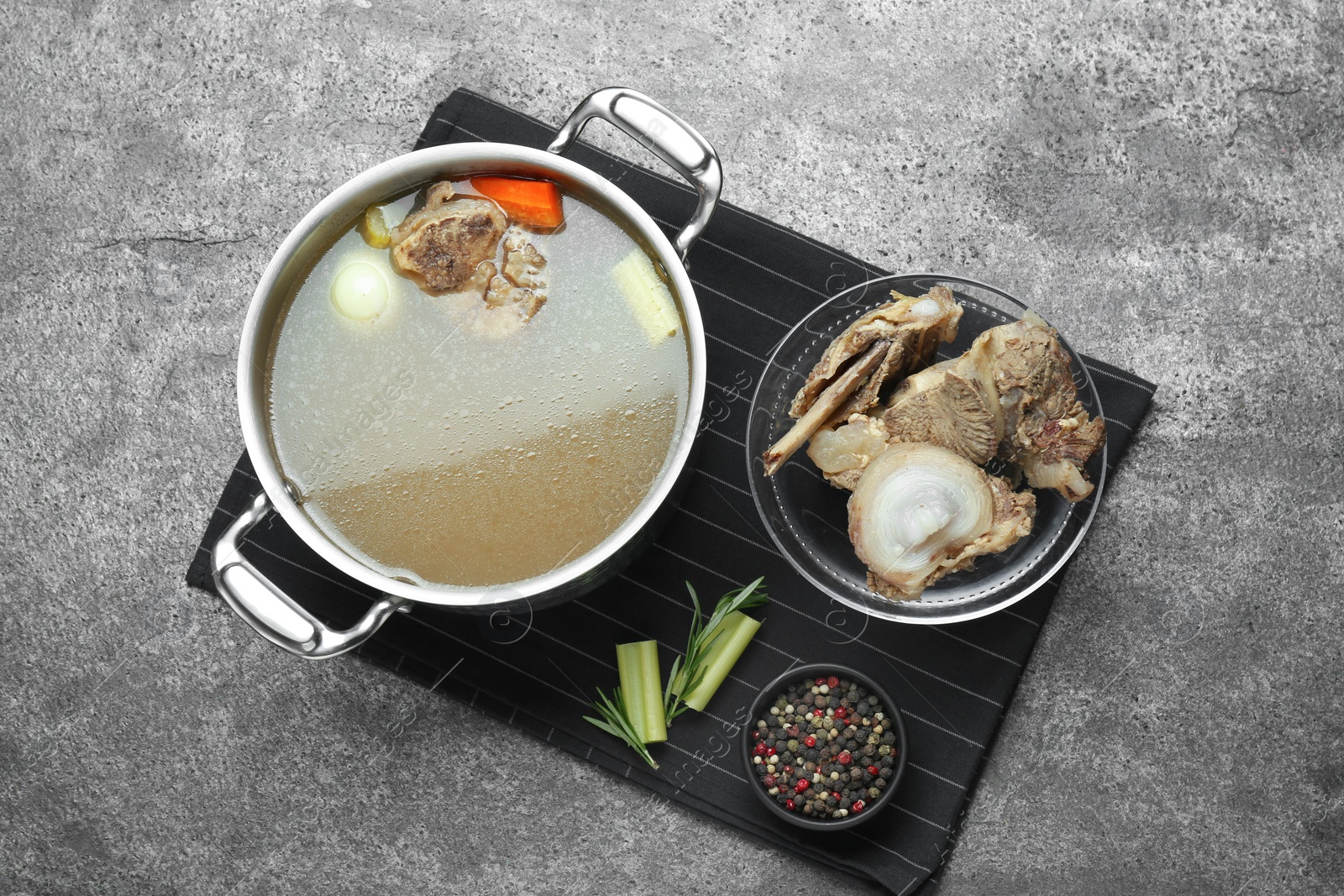 Photo of Pot with delicious bone broth and ingredients on grey table, flat lay